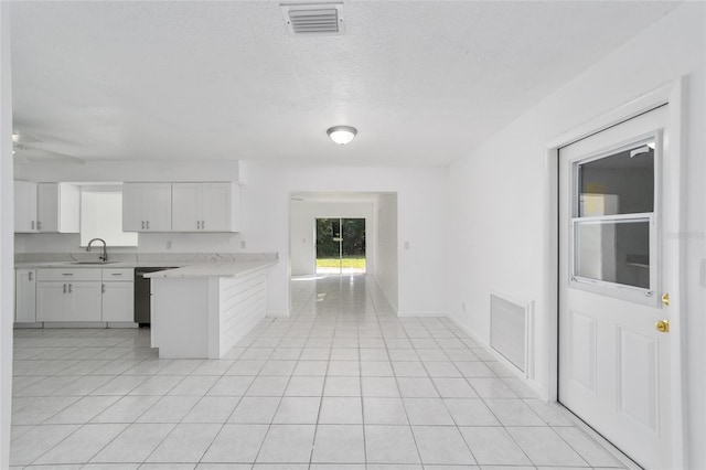 kitchen featuring stainless steel dishwasher, kitchen peninsula, light tile patterned floors, and white cabinets