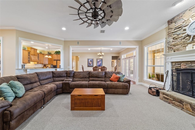 living room with a stone fireplace, crown molding, a chandelier, and light colored carpet