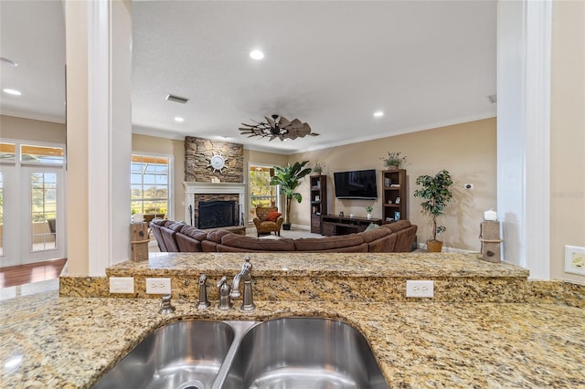 kitchen with a stone fireplace, ornamental molding, light stone countertops, and sink