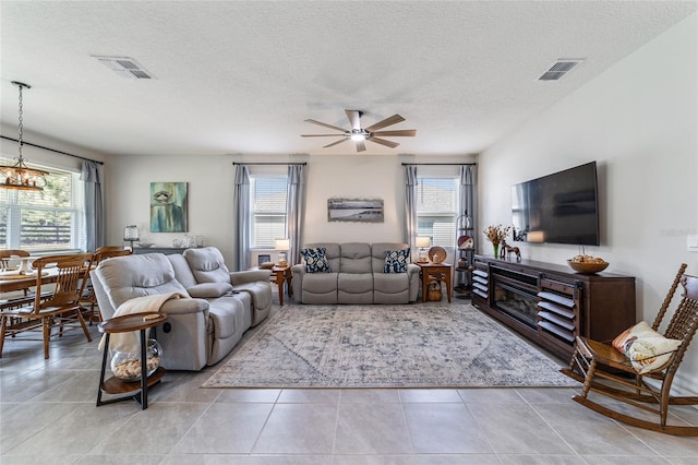 tiled living room with ceiling fan with notable chandelier and a textured ceiling