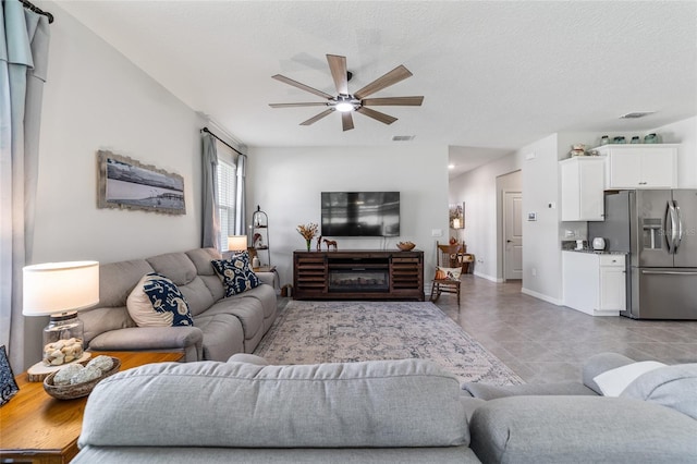 living room with ceiling fan, a textured ceiling, and light tile patterned floors