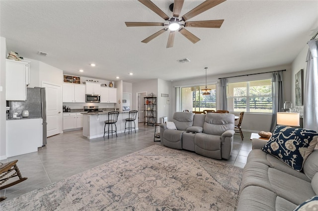 tiled living room featuring ceiling fan with notable chandelier and a textured ceiling