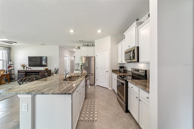 kitchen with sink, white cabinetry, a center island with sink, appliances with stainless steel finishes, and dark stone countertops