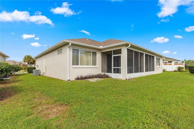rear view of house featuring stucco siding, a sunroom, central AC unit, and a yard