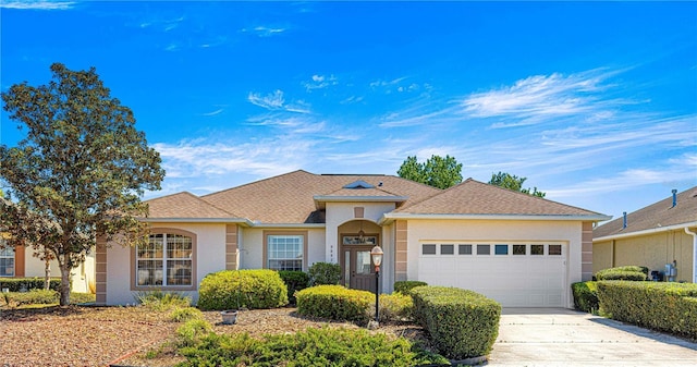 ranch-style home with a shingled roof, driveway, stucco siding, and an attached garage