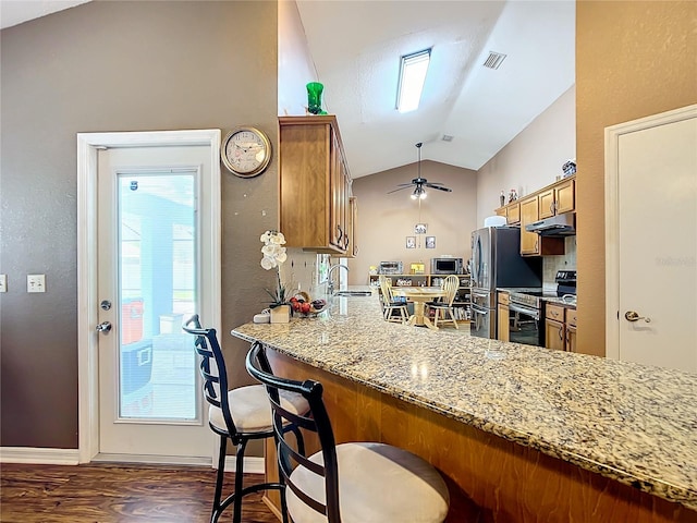 kitchen with light stone counters, kitchen peninsula, dark wood-type flooring, stainless steel appliances, and vaulted ceiling