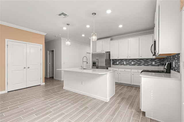 kitchen featuring light wood-type flooring, a center island with sink, stainless steel appliances, hanging light fixtures, and white cabinetry