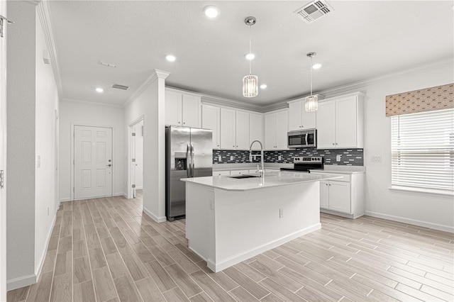 kitchen featuring an island with sink, stainless steel appliances, white cabinets, light hardwood / wood-style floors, and ornamental molding