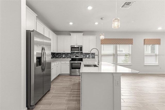 kitchen with sink, hanging light fixtures, appliances with stainless steel finishes, an island with sink, and white cabinetry