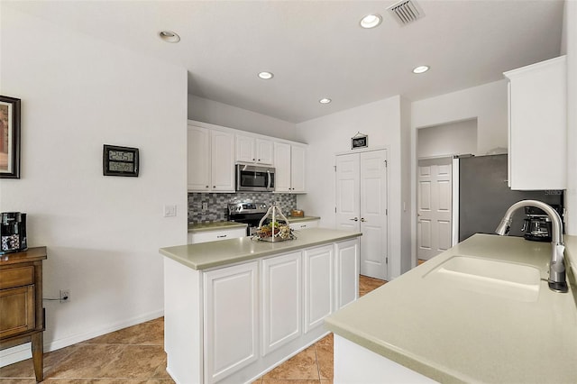 kitchen with sink, a kitchen island, backsplash, white cabinetry, and stainless steel appliances