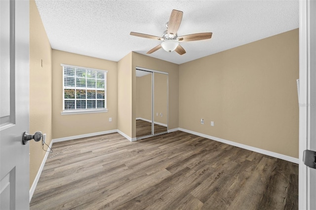 unfurnished bedroom featuring ceiling fan, a textured ceiling, a closet, and wood-type flooring