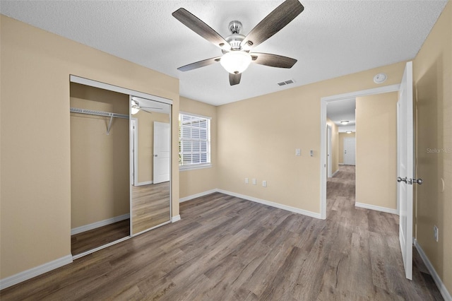 unfurnished bedroom with ceiling fan, a textured ceiling, a closet, and hardwood / wood-style floors