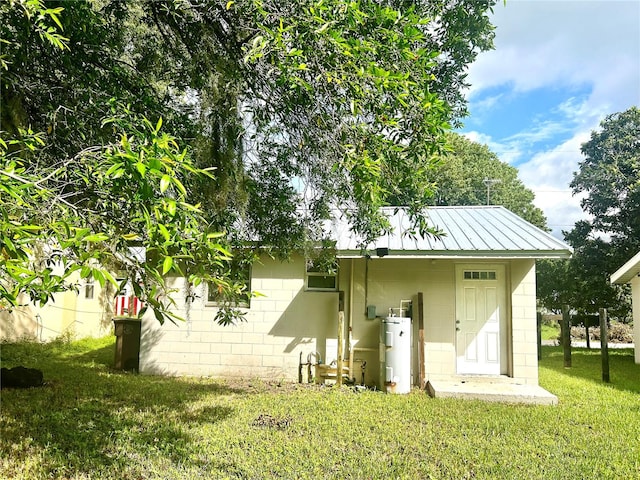 rear view of property with water heater, a lawn, and a storage unit