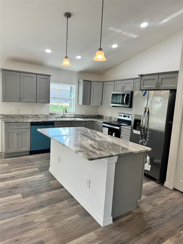 kitchen featuring light stone counters, a center island, vaulted ceiling, appliances with stainless steel finishes, and pendant lighting