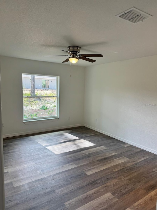 empty room featuring ceiling fan, dark wood-type flooring, and a textured ceiling