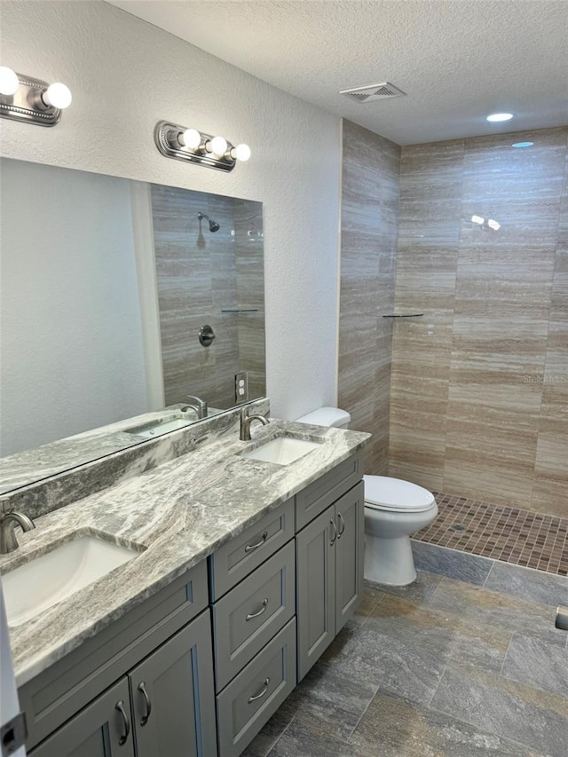 bathroom featuring vanity, a textured ceiling, toilet, and a tile shower