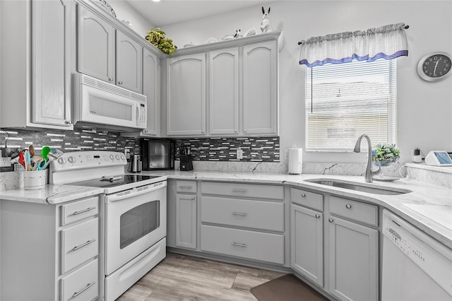 kitchen with light wood-type flooring, tasteful backsplash, gray cabinetry, white appliances, and sink