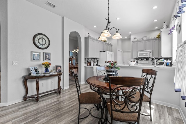 dining area with light hardwood / wood-style floors, plenty of natural light, and an inviting chandelier