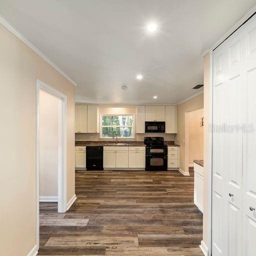 kitchen featuring white cabinetry, dark hardwood / wood-style flooring, black appliances, ornamental molding, and sink