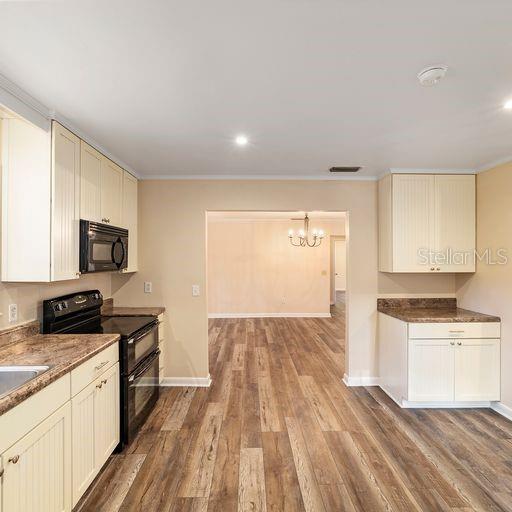 kitchen featuring black appliances, ornamental molding, wood-type flooring, and a notable chandelier