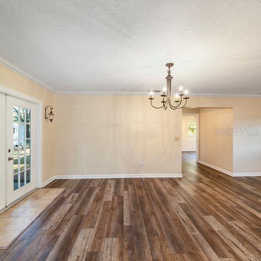 unfurnished room featuring ornamental molding, a chandelier, a textured ceiling, and dark hardwood / wood-style flooring