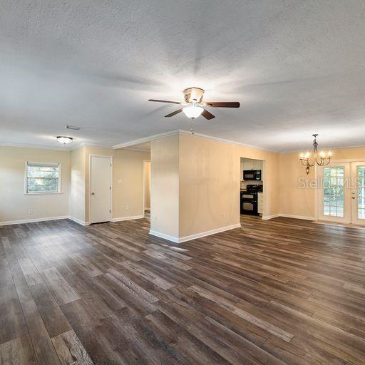 unfurnished living room with a textured ceiling, ceiling fan with notable chandelier, dark wood-type flooring, and a wealth of natural light