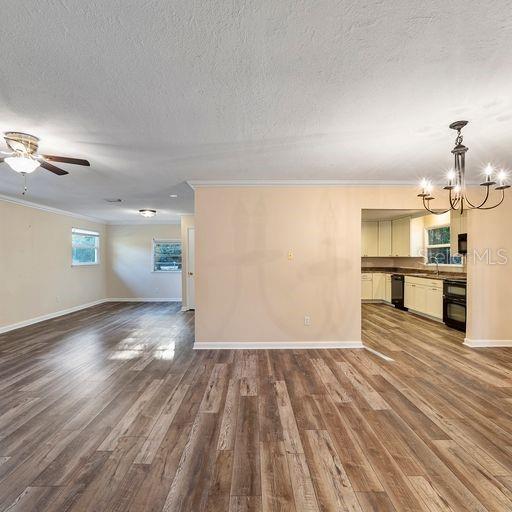 unfurnished living room featuring hardwood / wood-style flooring, ceiling fan with notable chandelier, ornamental molding, and a textured ceiling