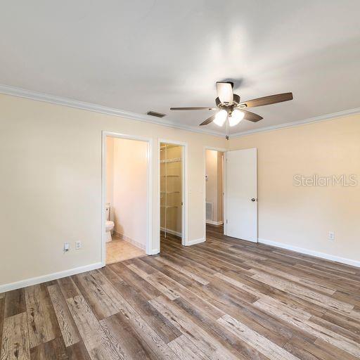 unfurnished bedroom featuring ensuite bathroom, hardwood / wood-style floors, crown molding, a spacious closet, and ceiling fan