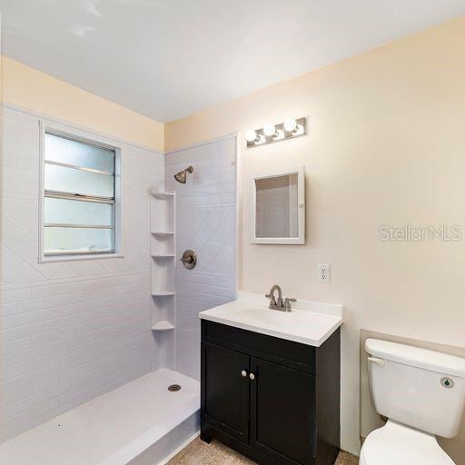 bathroom with a tile shower, vanity, and toilet