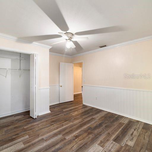 unfurnished bedroom with ceiling fan, ornamental molding, a closet, and dark wood-type flooring