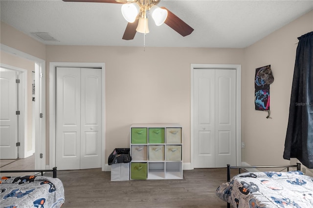 bedroom featuring ceiling fan, hardwood / wood-style flooring, two closets, and a textured ceiling