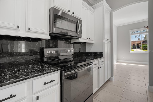 kitchen featuring light tile patterned flooring, stainless steel appliances, dark stone counters, white cabinets, and decorative backsplash