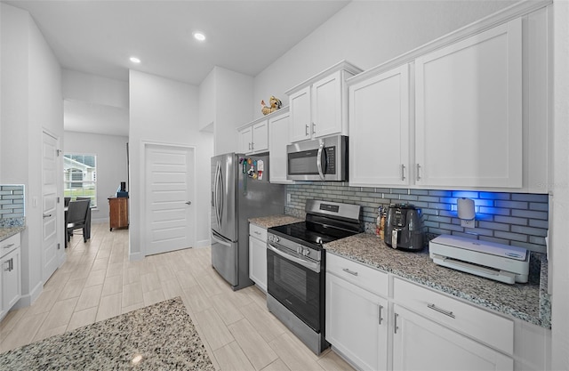 kitchen featuring white cabinets, light wood-type flooring, stainless steel appliances, and light stone countertops