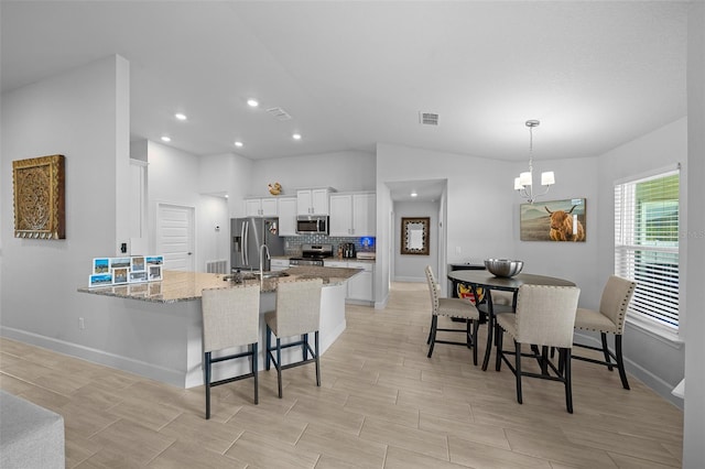 kitchen with white cabinetry, stainless steel appliances, a kitchen breakfast bar, light stone counters, and kitchen peninsula