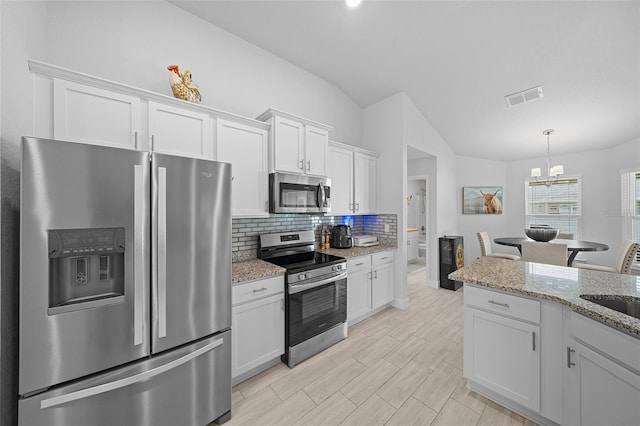 kitchen with light stone counters, stainless steel appliances, vaulted ceiling, an inviting chandelier, and white cabinetry