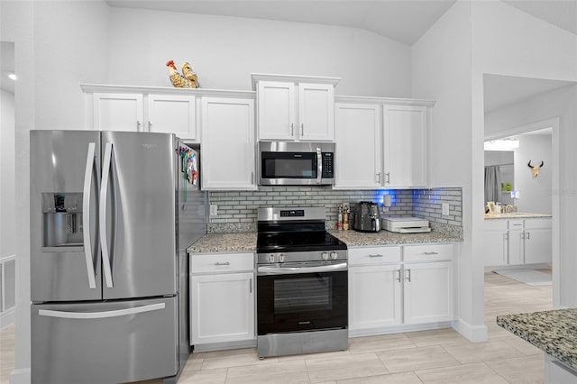 kitchen featuring light stone countertops, appliances with stainless steel finishes, white cabinetry, and vaulted ceiling