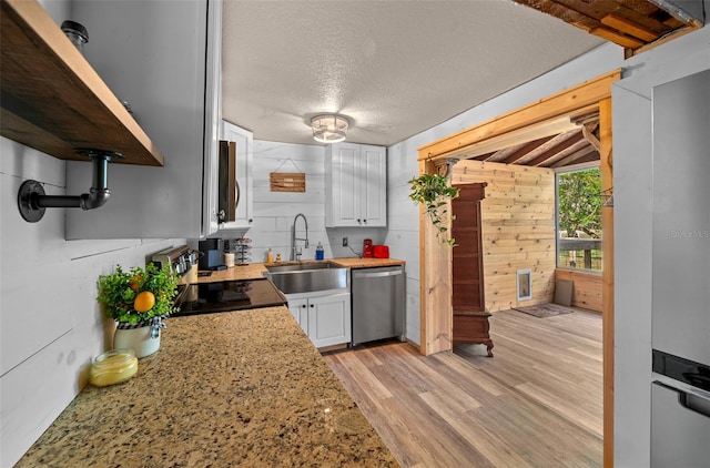 kitchen featuring dishwasher, light hardwood / wood-style floors, sink, white cabinets, and wooden walls