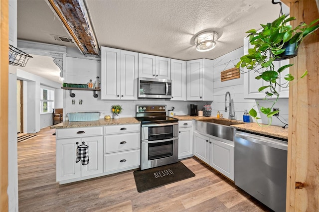 kitchen with light wood-type flooring, sink, white cabinetry, appliances with stainless steel finishes, and light stone countertops