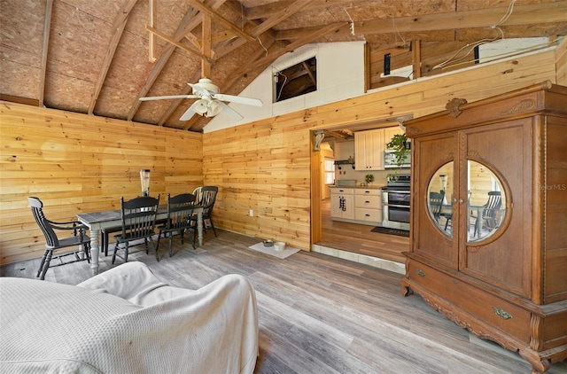 dining space featuring high vaulted ceiling, beamed ceiling, ceiling fan, hardwood / wood-style flooring, and wooden walls