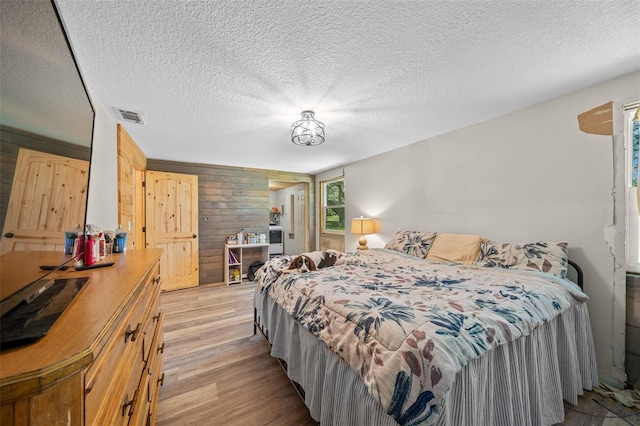 bedroom with a textured ceiling, light wood-type flooring, and wood walls