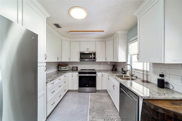 kitchen with light stone counters, sink, a textured ceiling, white cabinetry, and stainless steel appliances