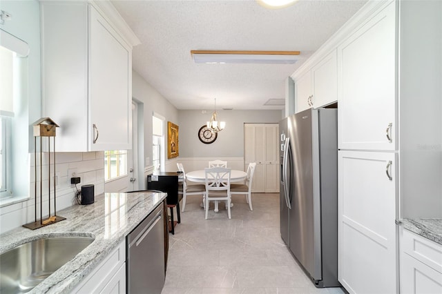 kitchen featuring light stone counters, white cabinets, hanging light fixtures, a textured ceiling, and stainless steel appliances