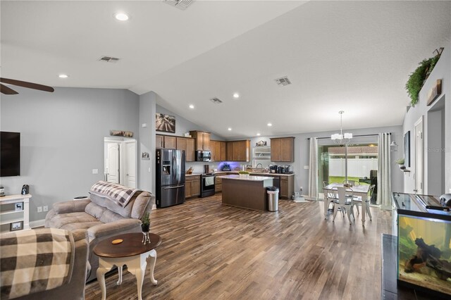 living room with sink, ceiling fan with notable chandelier, dark hardwood / wood-style floors, and vaulted ceiling