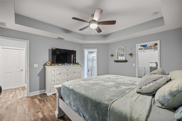 bedroom with ceiling fan, a raised ceiling, dark wood-type flooring, a closet, and a spacious closet