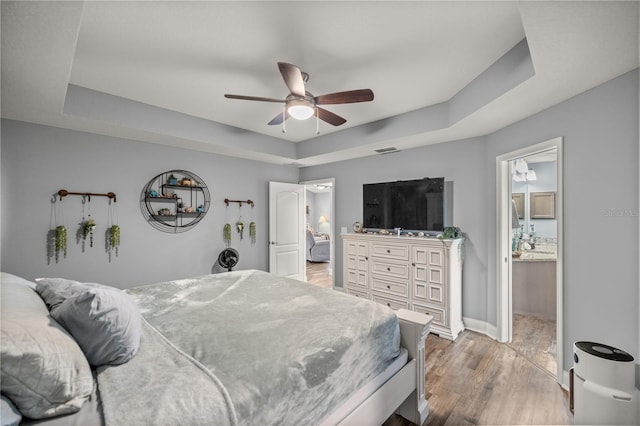 bedroom with light hardwood / wood-style floors, a tray ceiling, ceiling fan, and ensuite bathroom