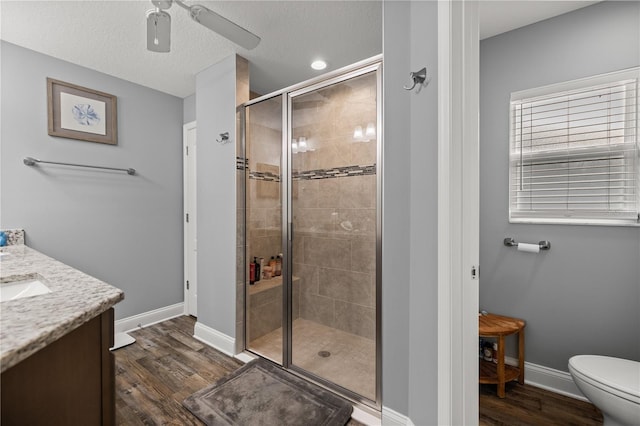 bathroom with hardwood / wood-style flooring, a shower with shower door, ceiling fan, vanity, and toilet