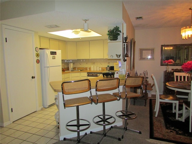 kitchen with kitchen peninsula, white fridge, white cabinetry, and a breakfast bar area