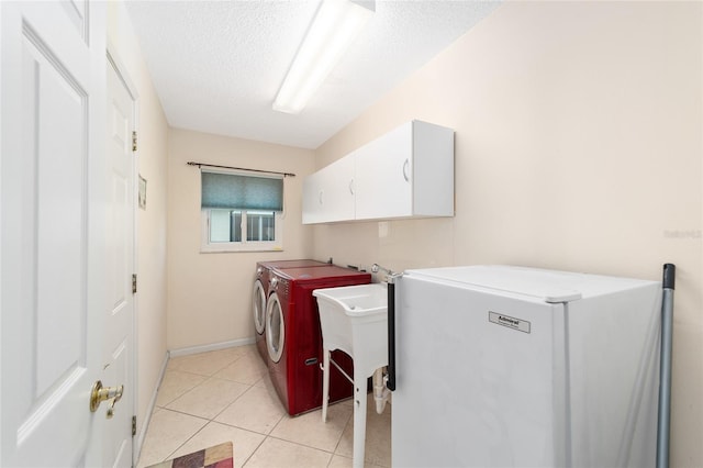 laundry room with a textured ceiling, washer and clothes dryer, light tile patterned floors, and cabinets