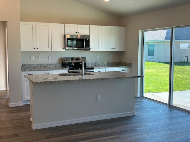 kitchen with light stone counters, stainless steel appliances, lofted ceiling, white cabinets, and an island with sink