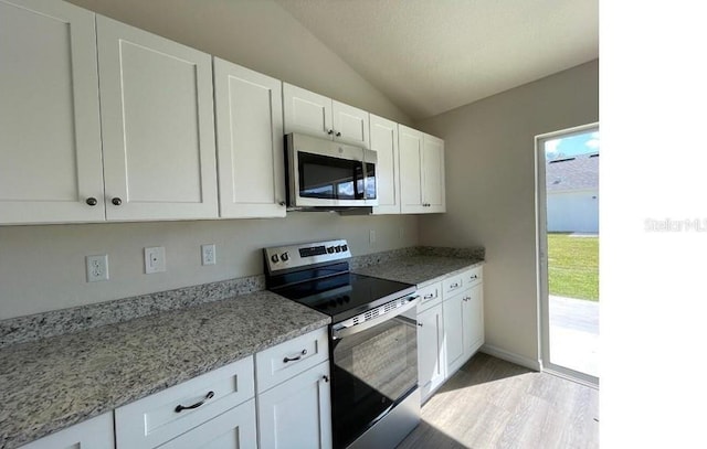 kitchen featuring stainless steel appliances, lofted ceiling, white cabinetry, and light stone counters